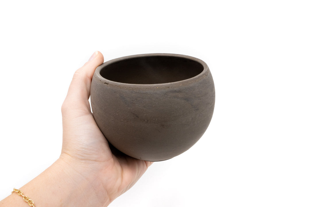 hand holding charcoal clay container