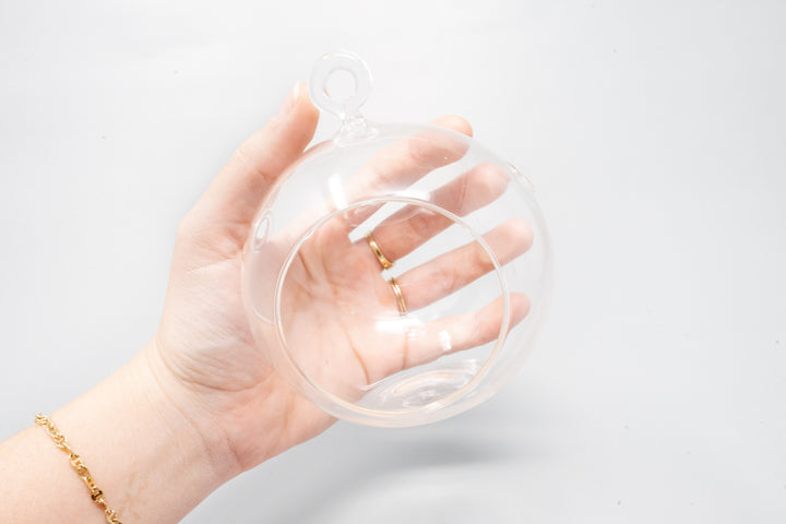 hand holding a glass globe terrarium with flat bottom and hook for hanging