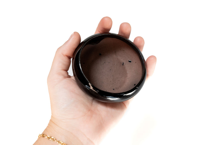 hand holding black glazed terracotta plant dish